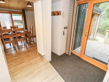 A dining area with wooden table and chairs next to a glass door leading to a wooden deck at Lodge 6 in Corfe Castle