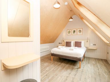 A bedroom with a double bed pillows framed pictures mirror and slanted ceiling at Lodge 6 in Corfe Castle