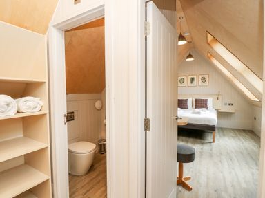 A bedroom with a bed and bedside tables next to a bathroom with a toilet and shelves with towels at Lodge 6 in Corfe Castle