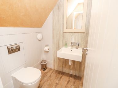 A small bathroom with a toilet a wall-mounted sink a mirror and wooden flooring at Lodge 6 in Corfe Castle