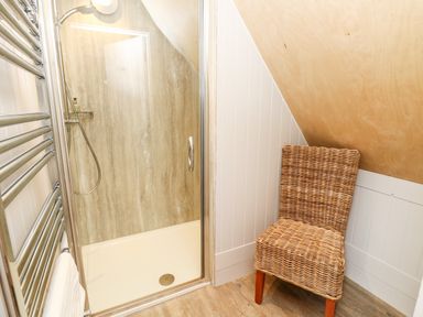 A shower enclosure with a glass door and a wicker chair next to it in a bathroom at Lodge 6 Corfe Castle