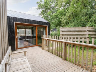 A wooden deck with a bench and railing outside a building with large glass sliding doors at Lodge 6 in Corfe Castle