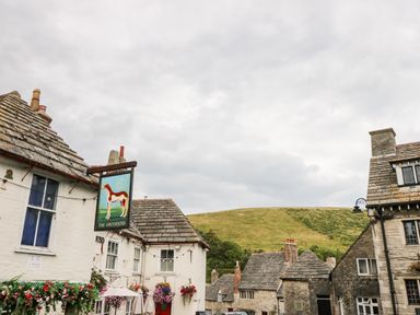 A street view with old stone buildings a sign for The Greyhound and a hill in the background at Lodge 6 in Corfe Castle