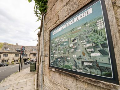 A street view showing a stone building with a village map of Corfe Castle Village mounted on the wall at Lodge 6 in Corfe Castle