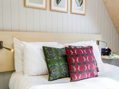 A bed with white pillows and butterfly patterned cushions with wall lamps at Lodge 9 in Corfe Castle