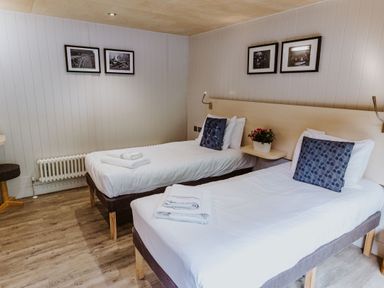A bedroom with two single beds each with folded towels and cushions a small table with a plant and framed pictures on walls at Lodge 11 in Corfe Castle
