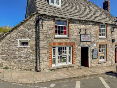 Stone building with windows and an open door and a sign reading village bakery on a street corner at Lodge 12 in Corfe Castle
