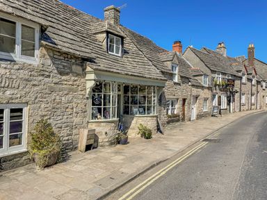 A street with stone buildings including a shop and a pub under a clear blue sky at Lodge 12 in Corfe Castle