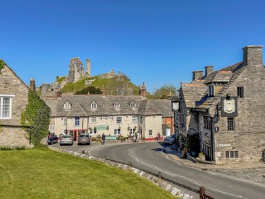 A village street with stone buildings cars and ruins of a castle on a hill in the background at Lodge 12 Corfe Castle