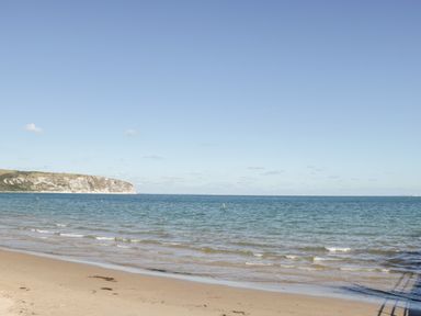 A sandy beach with small waves and a cliff in the distance at Lodge 12 in Corfe Castle