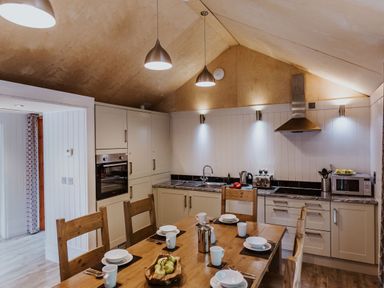 A kitchen with wooden dining table set for six and white cabinets at Lodge 12 in Corfe Castle