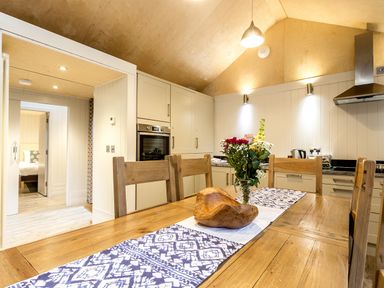 A kitchen with wooden dining table and chairs a flower vase and a wooden bowl on the table at Lodge 13 in Corfe Castle