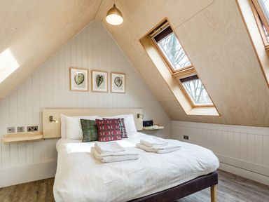 A bedroom with a double bed under slanted ceiling skylight windows and three leaf artwork at Lodge 13 in Corfe Castle