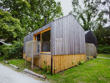 A wooden cabin with vertical planks and a large window surrounded by trees at Lodge 15 in Corfe Castle