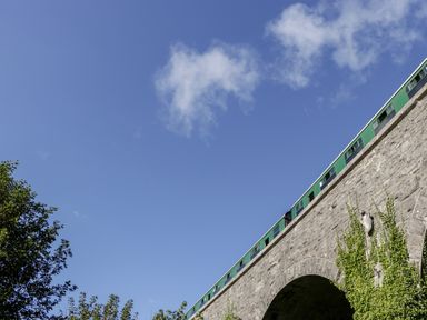 A green train on a stone bridge with blue sky and some trees below at Lodge 16 in Corfe Castle