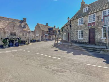 A street with stone buildings and shops including Bankes Arms and Castle Gemzones in Corfe Castle