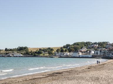 A beach with two people walking along the shore and buildings near the water at Lodge 17 in Corfe Castle