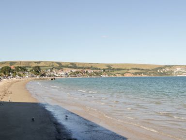 A beach with sand and small waves with houses and hills in the background at Lodge 17 in Corfe Castle