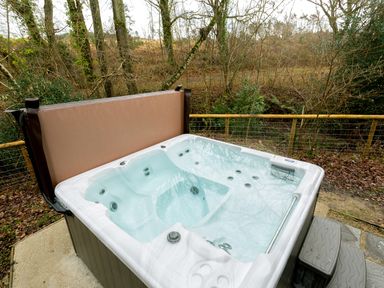 An outdoor hot tub with water and cover open next to a fence with trees behind at Lodge 19 in Corfe Castle