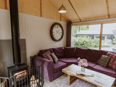 A living room with a purple sofa and wood stove at Lodge 19 in Corfe Castle