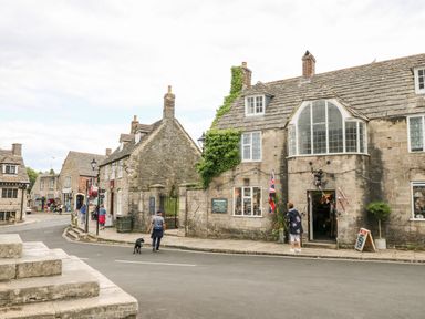A street view with stone buildings and people walking in Corfe Castle