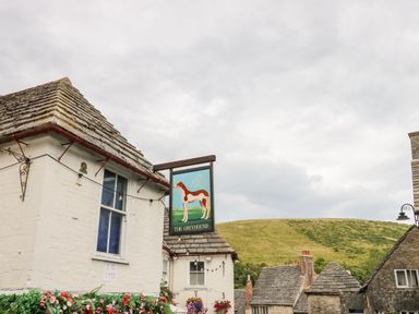 An exterior view of a building with a sign showing a greyhound and rooftops with a hill in the background at Lodge 20 in Corfe Castle