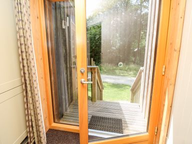 A wooden framed glass door leading to an outdoor wooden deck with stairs and a doormat at Lodge 21 in Corfe Castle