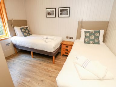 A bedroom with two single beds separated by a wooden nightstand and two framed pictures on the wall at Lodge 21 in Corfe Castle