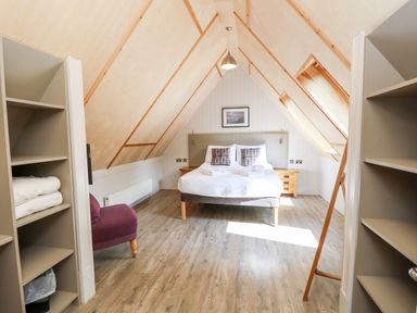 A bedroom with a double bed two bedside tables a purple chair shelves and skylight windows at Lodge 21 in Corfe Castle