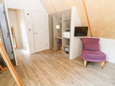 A room with wooden flooring a purple chair a wall-mounted television and open shelving at Lodge 21 in Corfe Castle