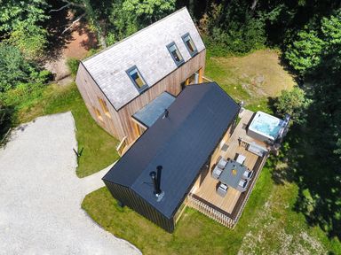 A wooden house with a black-roofed extension a deck with outdoor furniture and a hot tub surrounded by grass and trees at Lodge 22 in Corfe Castle