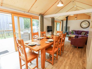A dining area with a wooden table set for six and a living room with purple seating and a clock on the wall at Lodge 22 in Corfe Castle