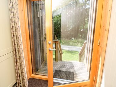 A wooden framed glass door opening to a small wooden deck with steps leading down to a grass area outside at Lodge 22 in Corfe Castle