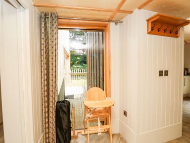 A wooden high chair near a glass door with curtains and a coat rack on the wall at Lodge 22 in Corfe Castle
