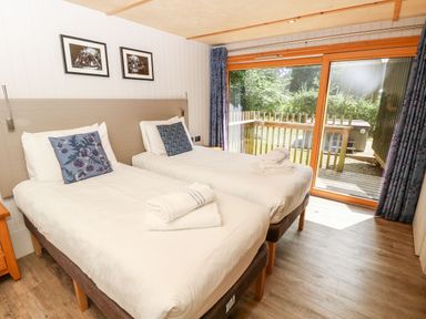 A bedroom with two single beds pillows and towels next to a sliding glass door with a view of a wooden deck and greenery at Lodge 22 in Corfe Castle