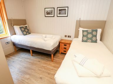 A bedroom with two single beds a wooden nightstand between the beds and framed pictures on the wall at Lodge 22 in Corfe Castle