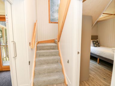 A hallway with carpeted stairs leading up and a bedroom with a bed visible at Lodge 22 Corfe Castle