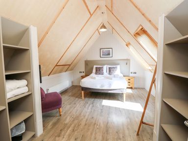 A bedroom with a double bed a purple armchair and wooden shelves in an attic room at Lodge 22 in Corfe Castle