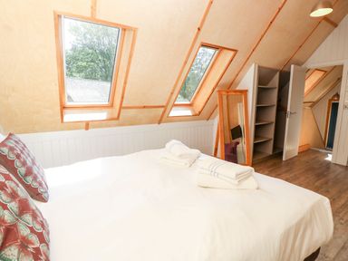 A bedroom with a bed and pillows under skylight windows a floor mirror an open closet and wooden flooring at Lodge 22 in Corfe Castle