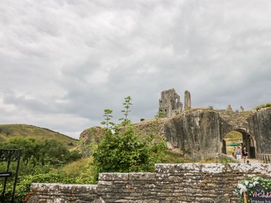 Ruins of an old stone castle with a large archway and surrounding greenery under a cloudy sky at Lodge 22 in Corfe Castle