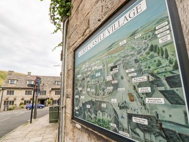 A village map mounted on a stone wall beside a sidewalk with a historic stone building and street signs at Lodge 22 in Corfe Castle