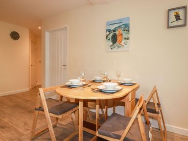 A dining area with a wooden table set for four and four wooden chairs with cushions at Falcon House in Tintagel