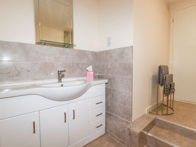 A bathroom sink with white cabinetry a mirror and towels on a rack near steps at Falcon House in Tintagel