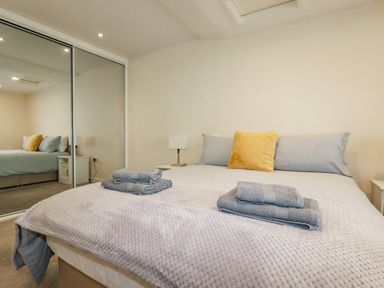 A bedroom with a bed covered in blankets and towels a bedside table with a lamp and mirrored sliding closet doors at Falcon House in Tintagel