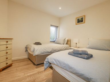 A bedroom with two single beds two towels on each bed a nightstand with a lamp a window and a chest of drawers at Falcon House in Tintagel