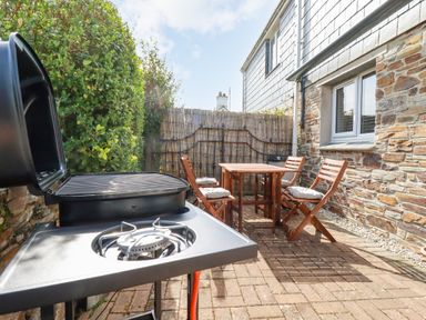 An outdoor patio area with a gas grill and a wooden table with four chairs at Falcon House in Tintagel