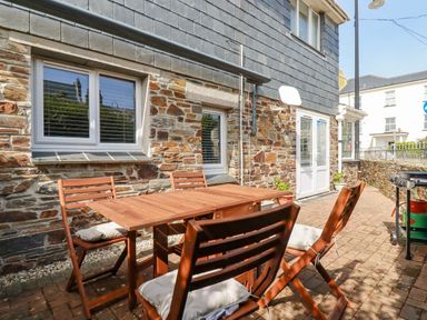 An outdoor patio with wooden table and chairs and a barbecue grill at Falcon House in Tintagel