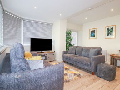 A living room with two gray sofas a television on a stand and framed pictures on the wall at Falcon House in Tintagel
