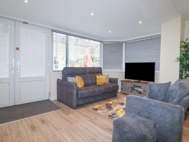 A living room with two gray sofas a television on a wooden stand and a rug at Falcon House in Tintagel