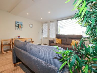 A living room with two sofas, a small table with chairs, wall art, and a large window with blinds at Falcon House in Tintagel